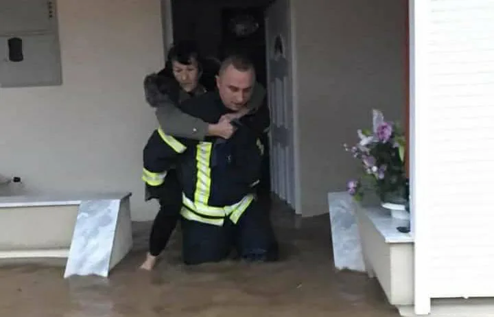Zjarrfikësi duke larguar të moshuarën nga shtëpia që iu përmbyt nga uji